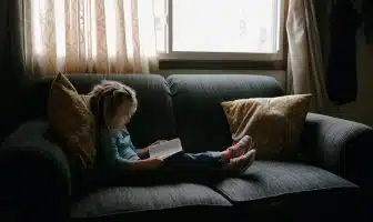 girl reading book sitting on sofa